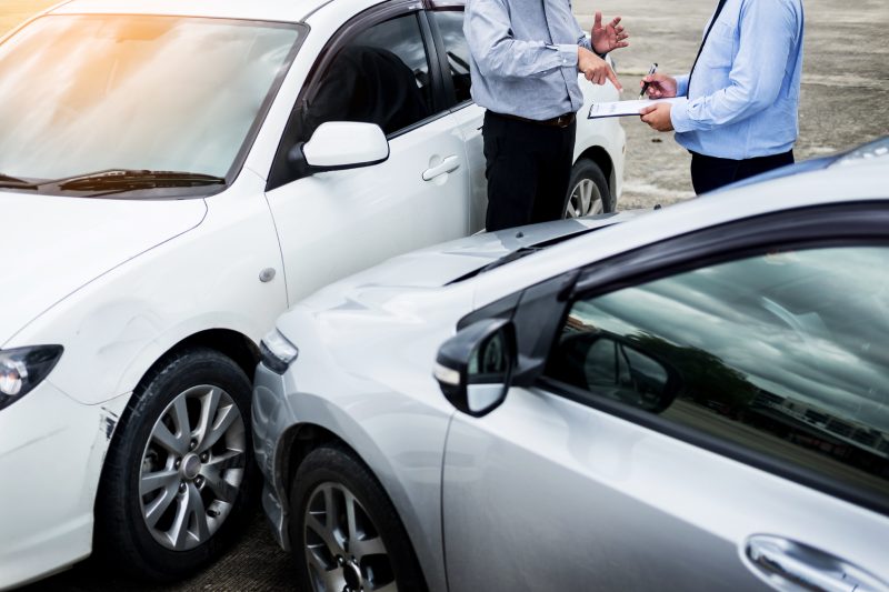 Insurance agent writing on clipboard while examining car after accident claim being assessed and processed