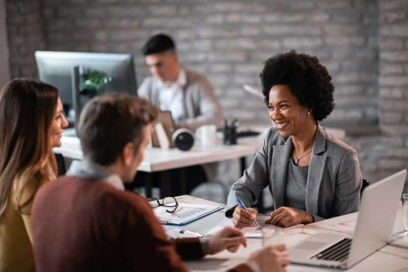 Happy African American financial advisor talking to a couple about their future investment during a meeting in the office.