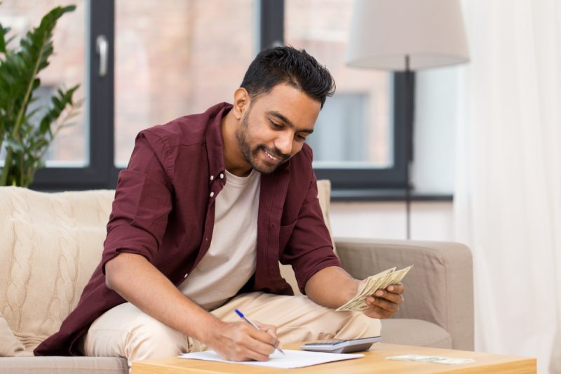 business, finances, accounting and people concept - man with money and calculator filling papers at home