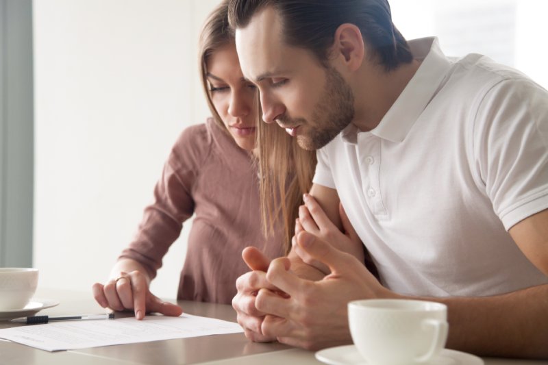 Serious couple studying contract agreement, reading terms and conditions attentively before signing, husband and wife calculating domestic bills, considering mortgage loan offer, health insurance