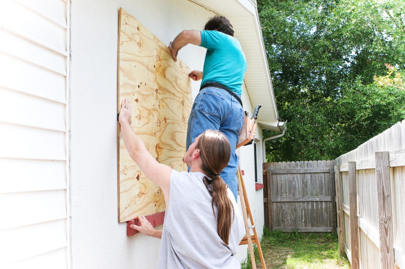 Teenage son helping his father board up the windows of their house in preparation for a hurricane.