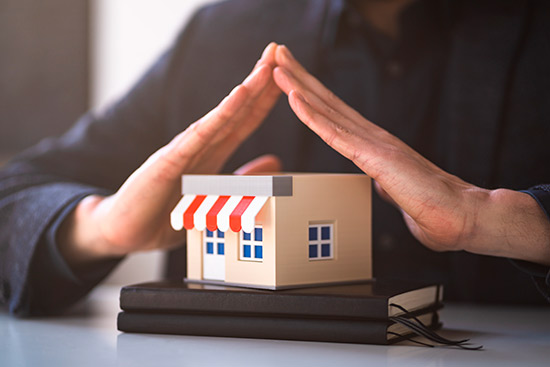 Businessman offering a small house model on books, representing the importance of hurricane preparedness for small businesses.