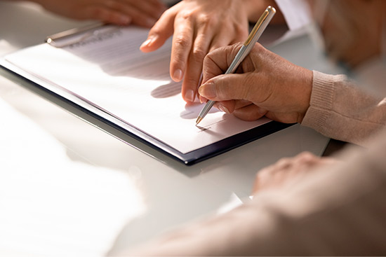 Individual signing a document on a table, representing the decision-making process for whole life insurance plans.