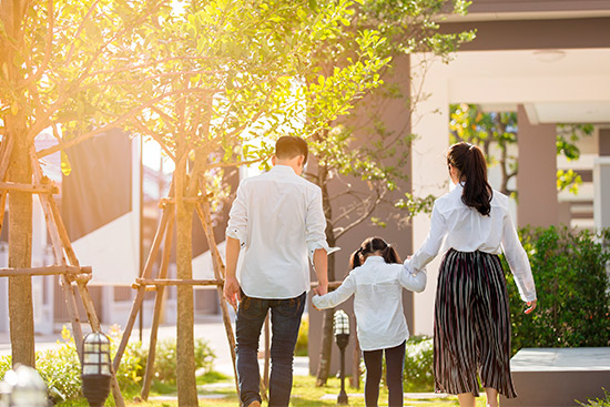 A family strolls on a grassy area beside a house, representing unity and the need for whole life insurance for protection.