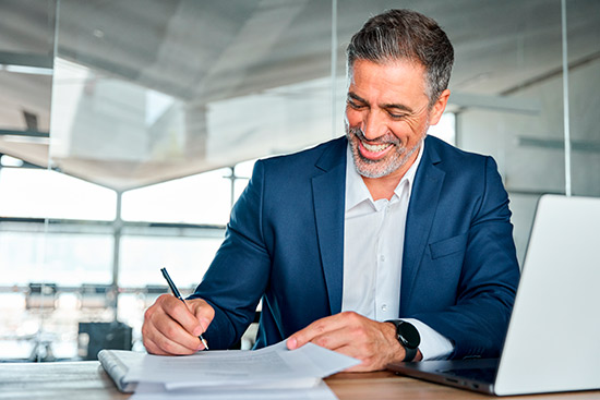A man in a suit smiles while writing, symbolizing insurance services for Midland commercial property owners.