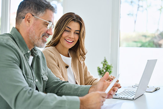 A smiling man and woman look at a laptop, discussing car insurance options in Laredo, TX.
