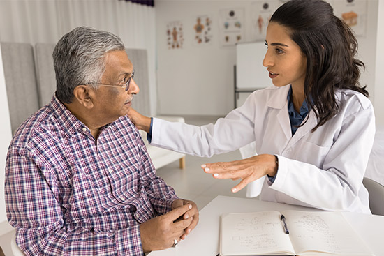 A doctor discussing health insurance costs with an elderly man in a medical office setting.