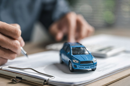 A man notes down information on paper while a car model sits next to him, focusing on affordable car insurance in McAllen.