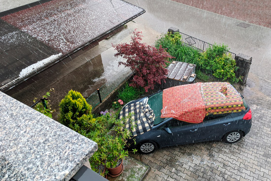 Car covered in blankets during strong hail storm. Car protection against hail during stormy weather