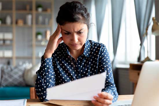 Indian woman sit at desk hold document read paper letter feels disappointed shocked by bad news. Financial trouble bank debt notice, medical test results health problems, huge domestic bills concept