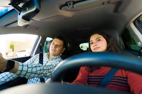 Hispanic dad teaching his teenage daughter to drive a car, helping her learn road safety